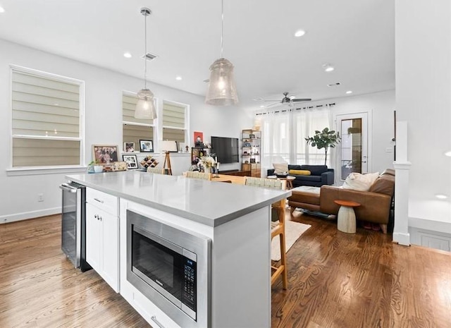 2753 Clinton Dr, Houston, TX 77020 - kitchen with stainless steel microwave, wine cooler, white cabinetry, a kitchen island, and wood finished floors