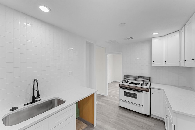 4715 Engleford St, Houston, TX 77026 - kitchen featuring white range with gas stovetop, light wood finished floors, decorative backsplash, white cabinets, and recessed lighting