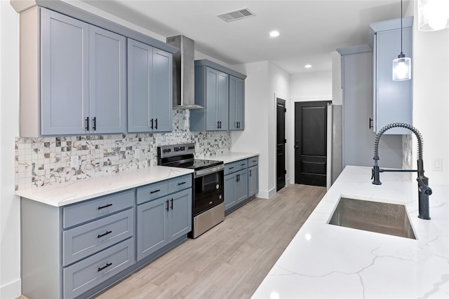 8136 Chateau St, Houston, TX 77028 - kitchen with stainless steel range with electric cooktop, wall chimney exhaust hood, light wood-style floors, light stone counters, and tasteful backsplash