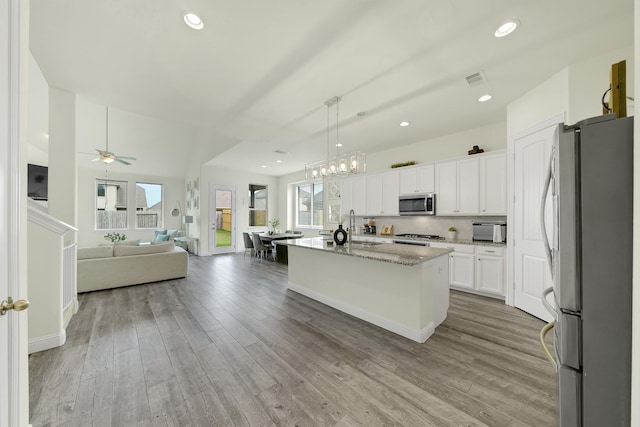 2810 Parkside Village Ln, Pearland, TX 77581 - kitchen featuring appliances with stainless steel finishes, open floor plan, white cabinets, light stone countertops, and wood finished floors
