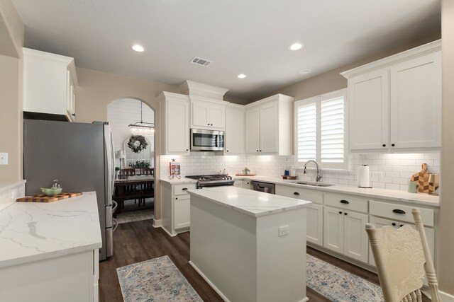 1803 Twin Oaks Cir, Brenham, TX 77833 - kitchen with stainless steel appliances, arched walkways, decorative backsplash, dark wood finished floors, and white cabinetry