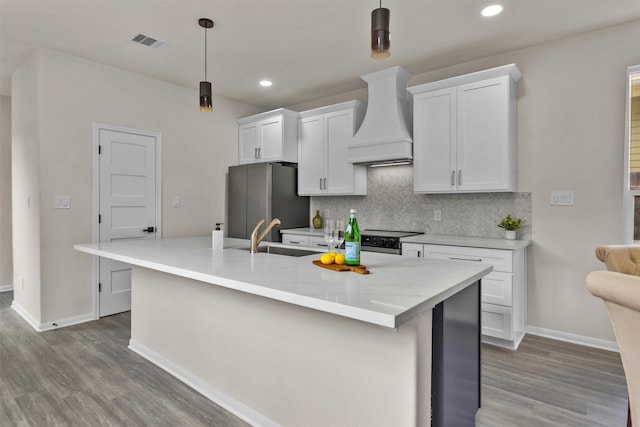 2413 Harlem St, Houston, TX 77020 - kitchen with custom range hood, freestanding refrigerator, wood finished floors, an island with sink, and recessed lighting