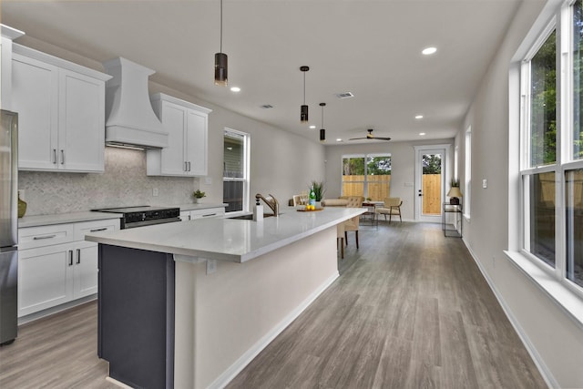 2413 Harlem St, Houston, TX 77020 - kitchen featuring custom exhaust hood, black electric range, wood finished floors, an island with sink, and tasteful backsplash
