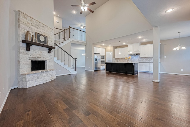 6518 Nicholas Trl, Sugar Land, TX 77479 - unfurnished living room featuring a ceiling fan, a stone fireplace, dark wood finished floors, stairway, and a towering ceiling