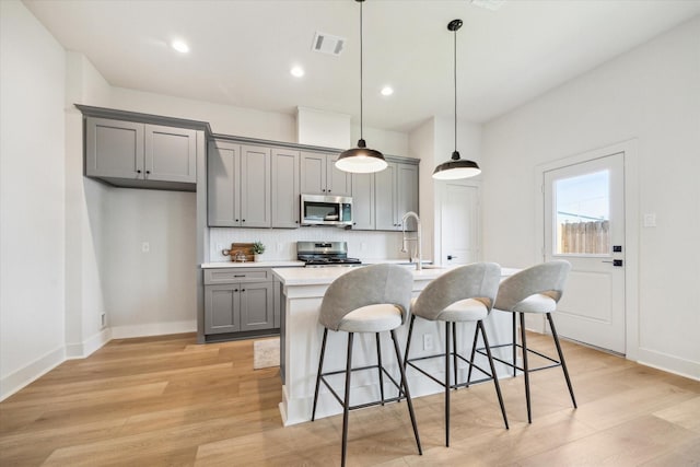 5256 Texas St, Houston, TX 77011 - kitchen with gray cabinets, appliances with stainless steel finishes, light wood finished floors, decorative backsplash, and a breakfast bar