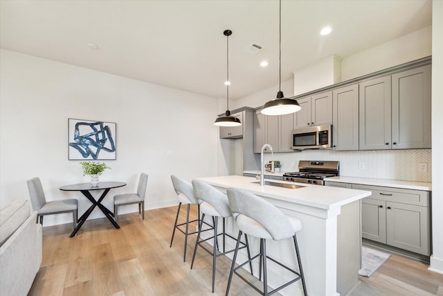 5256 Texas St, Houston, TX 77011 - kitchen featuring stainless steel appliances, gray cabinets, a breakfast bar, tasteful backsplash, and a kitchen island with sink