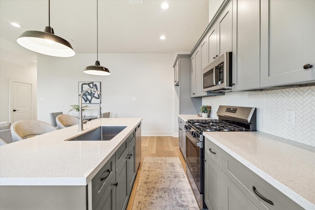 5256 Texas St, Houston, TX 77011 - kitchen featuring stainless steel appliances, gray cabinets, tasteful backsplash, light wood-style flooring, and a kitchen island with sink