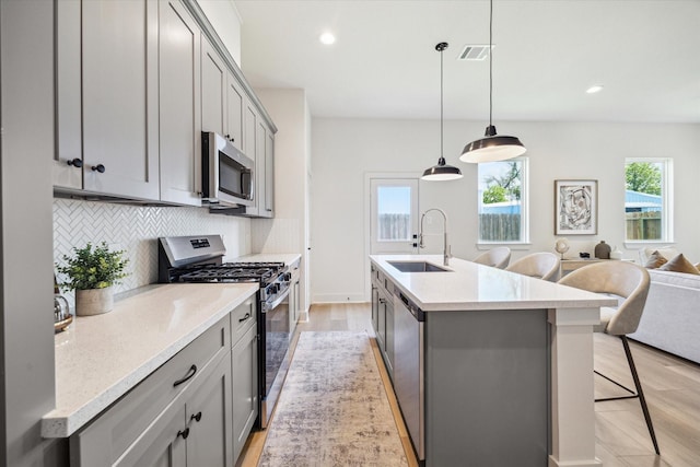 5256 Texas St, Houston, TX 77011 - kitchen with stainless steel appliances, gray cabinets, a kitchen island with sink, decorative backsplash, and a breakfast bar