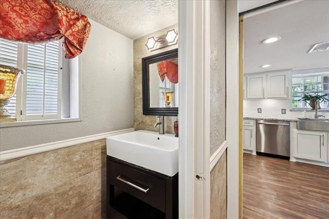 3231 Charles Ave, Groves, TX 77619 - bathroom with a textured wall, vanity, a textured ceiling, wood finished floors, and a wainscoted wall