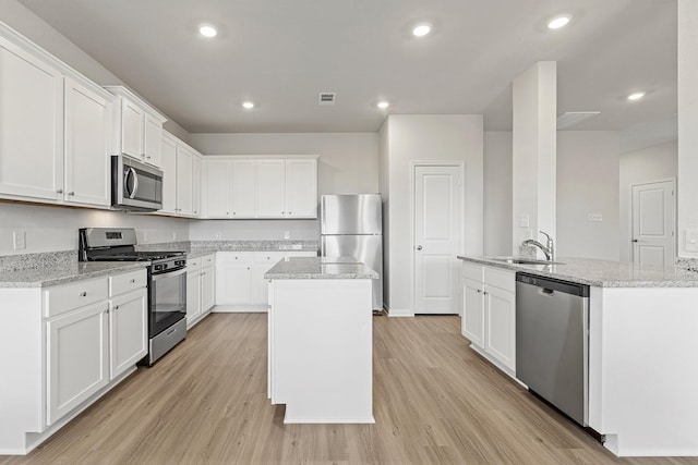 10811 Bright Beacon Dr, Beasley, TX 77417 - kitchen with stainless steel appliances, an island with sink, light wood finished floors, white cabinets, and recessed lighting