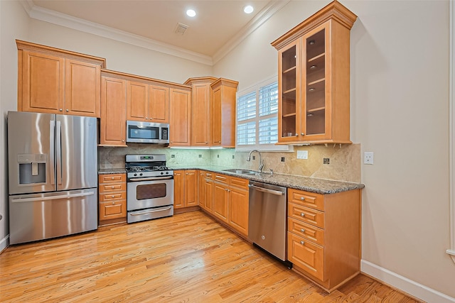 2616 Helena St, Houston, TX 77006 - kitchen featuring appliances with stainless steel finishes, ornamental molding, dark stone counters, light wood-style floors, and glass insert cabinets