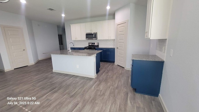 10627 Great Basin Dr, Rosharon, TX 77583 - kitchen featuring stainless steel appliances, backsplash, wood finished floors, white cabinetry, and an island with sink