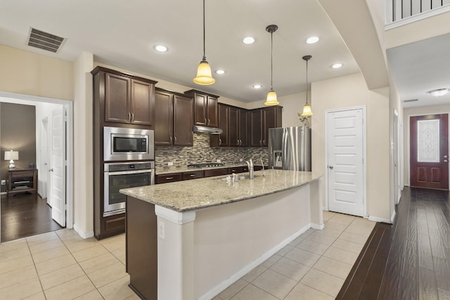 5314 Belle Manor Ln, Sugar Land, TX 77479 - kitchen with stainless steel appliances, under cabinet range hood, dark brown cabinets, light tile patterned floors, and backsplash