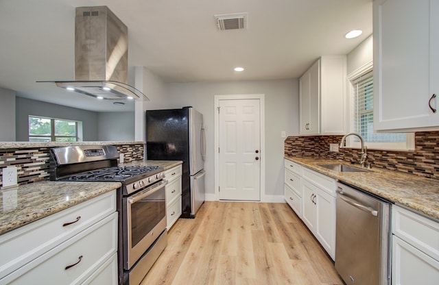 4914 W 43rd St, Houston, TX 77092 - kitchen with stainless steel appliances, island range hood, tasteful backsplash, light wood-type flooring, and white cabinets