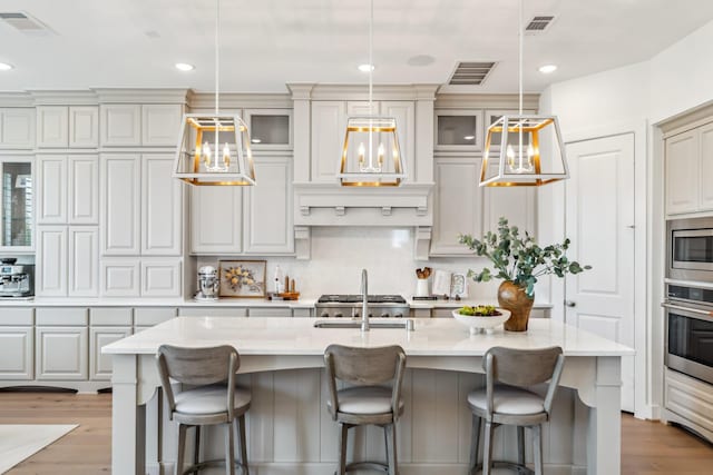 21514 Sunny Riverbank Cir, Cypress, TX 77433 - kitchen with appliances with stainless steel finishes, light countertops, light wood-style flooring, glass insert cabinets, and a breakfast bar area