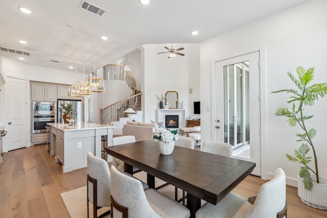 21514 Sunny Riverbank Cir, Cypress, TX 77433 - dining space with stairway, light wood-style flooring, a glass covered fireplace, recessed lighting, and ceiling fan