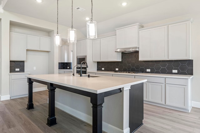 916 Wormwood Dr, League City, TX 77573 - kitchen with a kitchen island with sink, decorative backsplash, light wood-type flooring, a breakfast bar, and recessed lighting