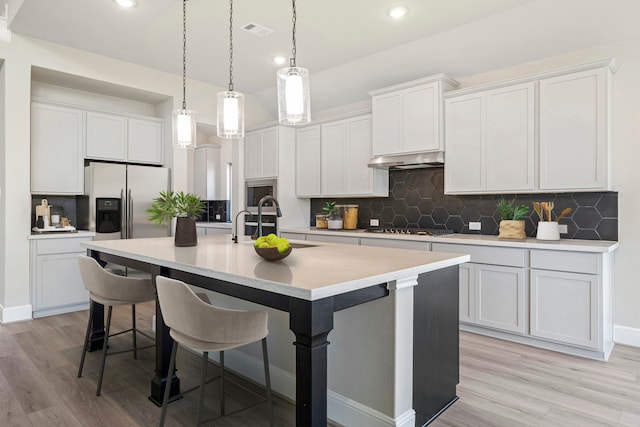 916 Wormwood Dr, League City, TX 77573 - kitchen with stainless steel appliances, an island with sink, light wood finished floors, a kitchen breakfast bar, and decorative backsplash