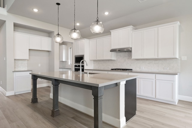 910 Hooks Trl, League City, TX 77573 - kitchen with stainless steel appliances, under cabinet range hood, tasteful backsplash, a center island with sink, and light wood-style floors