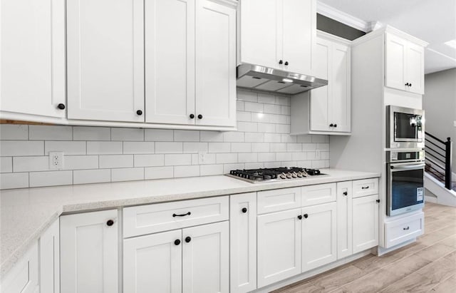 427 Rd 66111, Dayton, TX 77535 - kitchen with stainless steel appliances, under cabinet range hood, light wood finished floors, white cabinetry, and tasteful backsplash