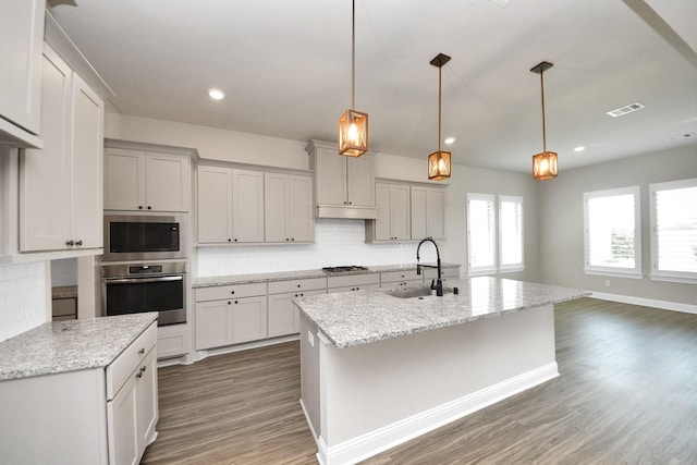 1831 Golden Cape Dr, Katy, TX 77494 - kitchen with stainless steel appliances, decorative backsplash, wood finished floors, light stone countertops, and a kitchen island with sink