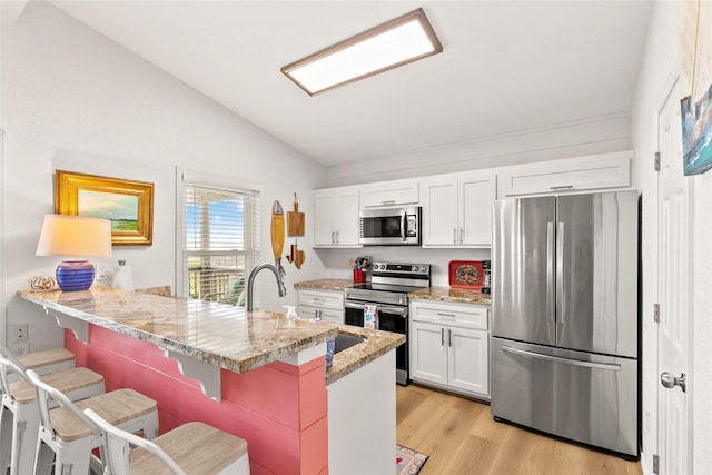 4630 Blue Water Hwy, Freeport, TX 77541 - kitchen with stainless steel appliances, vaulted ceiling, a breakfast bar area, white cabinets, and light wood-type flooring