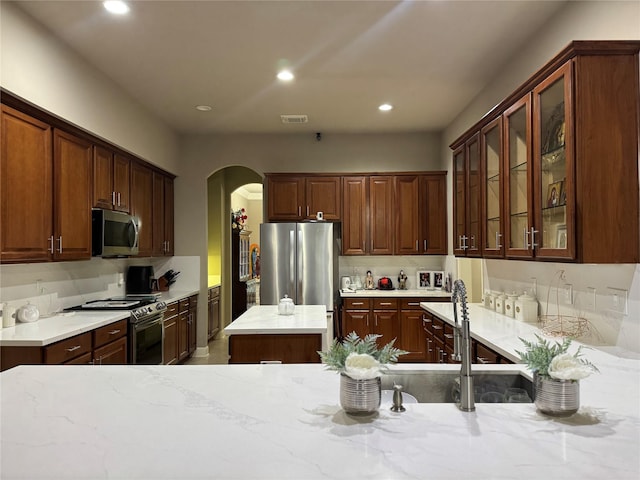 17907 Camp Cove Dr, Cypress, TX 77429 - kitchen featuring stainless steel appliances, arched walkways, recessed lighting, glass insert cabinets, and light stone counters