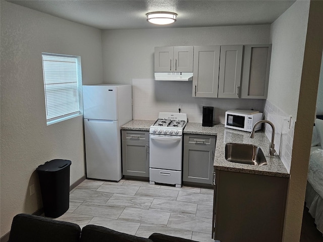 208 W 2nd St, Sweeny, TX 77480 - kitchen with white appliances, gray cabinets, under cabinet range hood, tasteful backsplash, and light stone countertops