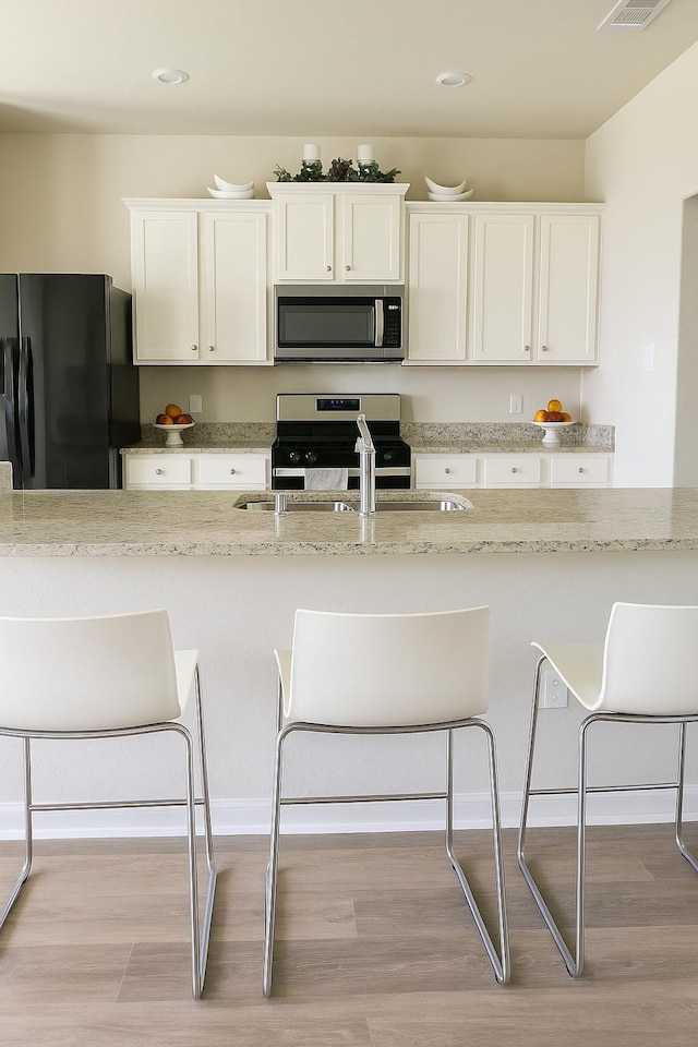 11407 Prairie Walk Dr, Houston, TX 77048 - kitchen featuring appliances with stainless steel finishes, light wood finished floors, a kitchen breakfast bar, light stone counters, and recessed lighting