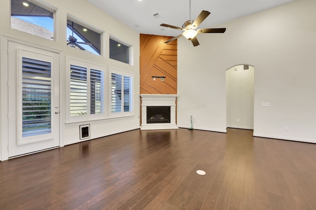 15 Floral Hills Ln, Fulshear, TX 77441 - unfurnished living room featuring a ceiling fan, a fireplace with raised hearth, high vaulted ceiling, wood finished floors, and arched walkways