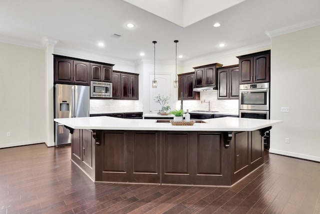 15 Floral Hills Ln, Fulshear, TX 77441 - kitchen with appliances with stainless steel finishes, a spacious island, light countertops, dark brown cabinets, and under cabinet range hood