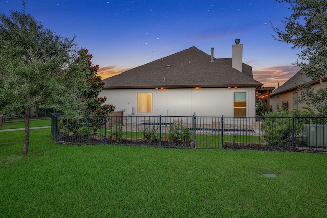 15 Floral Hills Ln, Fulshear, TX 77441 - back of house at dusk featuring a chimney, roof with shingles, and stucco siding