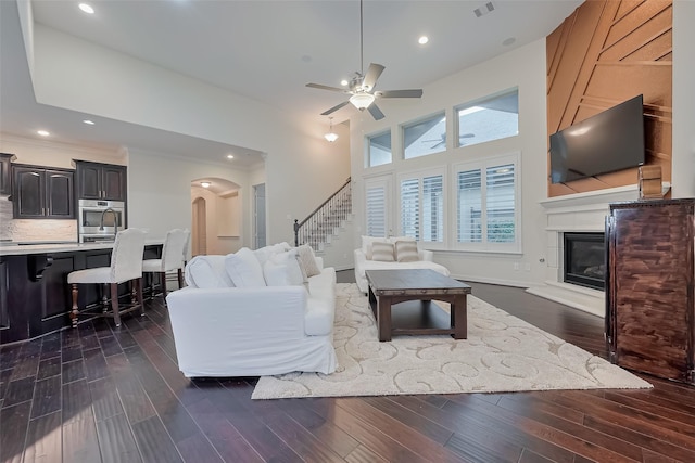 15 Floral Hills Ln, Fulshear, TX 77441 - living room with a glass covered fireplace, a ceiling fan, dark wood-type flooring, stairway, and arched walkways