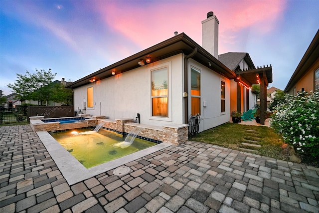 15 Floral Hills Ln, Fulshear, TX 77441 - back of house at dusk featuring a fenced backyard, a chimney, a patio, and stucco siding