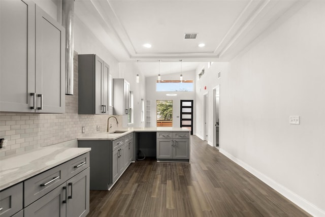 4817 Los Angeles St, Houston, TX 77026 - kitchen featuring gray cabinets, a peninsula, decorative backsplash, dark wood-style flooring, and light stone counters