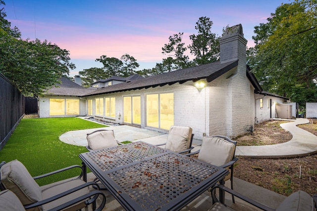 12422 Cobblestone Dr, Houston, TX 77024 - back of house at dusk featuring a chimney, brick siding, outdoor dining space, a patio, and a shingled roof