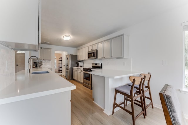17814 Placid Oak Ct, Cypress, TX 77433 - kitchen featuring stainless steel appliances, a kitchen bar, a peninsula, backsplash, and light wood finished floors