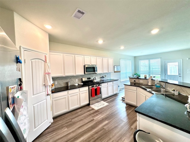 18802 Verdura Dr, New Caney, TX 77357 - kitchen featuring appliances with stainless steel finishes, wood finished floors, white cabinets, dark countertops, and recessed lighting