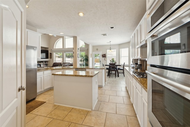 10906 Silverado Trace Dr, Houston, TX 77095 - kitchen with appliances with stainless steel finishes, a textured ceiling, a center island, white cabinetry, and hanging light fixtures