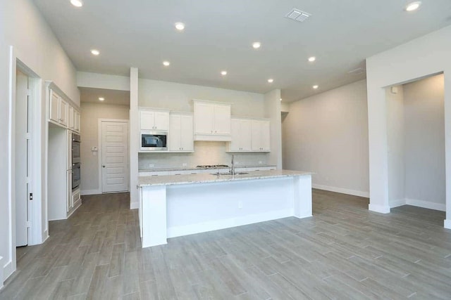 29838 Beth Ter, Fulshear, TX 77441 - kitchen with appliances with stainless steel finishes, light wood-style floors, a kitchen island with sink, white cabinets, and recessed lighting