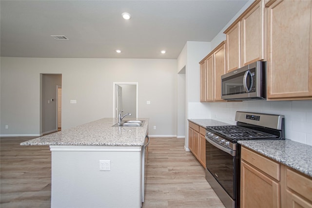 2926 Grand Hawthorne Rd, Conroe, TX 77385 - kitchen with appliances with stainless steel finishes, light brown cabinetry, light wood-type flooring, a kitchen island with sink, and backsplash