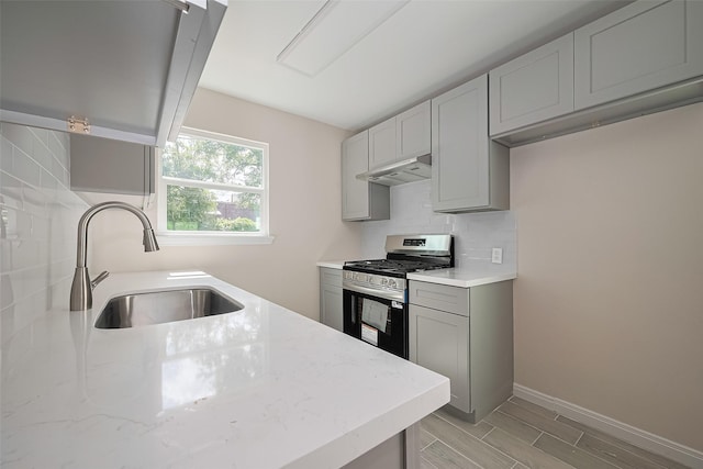 11311 Raincove Dr, Houston, TX 77016 - kitchen featuring gas stove, under cabinet range hood, decorative backsplash, light stone countertops, and gray cabinets
