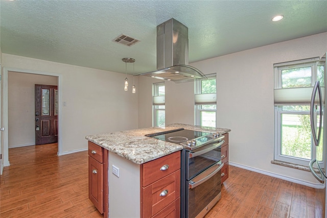 25418 Sugar Valley Ln, Spring, TX 77373 - kitchen featuring appliances with stainless steel finishes, island range hood, light wood-type flooring, brown cabinets, and light stone counters