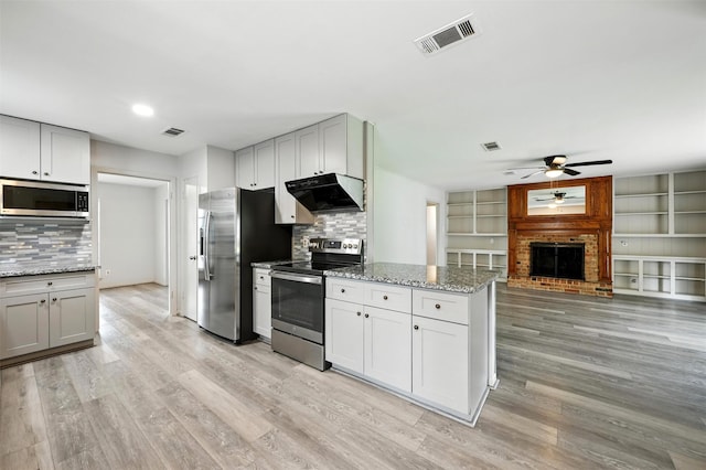 8503 Leader St, Houston, TX 77036 - kitchen featuring stainless steel appliances, under cabinet range hood, ceiling fan, a fireplace, and light wood-style floors