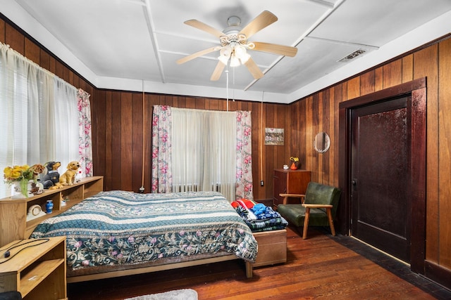 600 Brazos St, Glidden, TX 78943 - bedroom featuring dark wood-style floors, wooden walls, and a ceiling fan