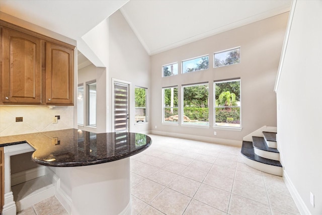 5215 Eagle Pointe Ct, Sugar Land, TX 77479 - kitchen with ornamental molding, dark stone countertops, light tile patterned floors, brown cabinetry, and high vaulted ceiling