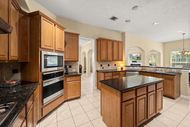 18718 Glenn Haven Estates Dr, Spring, TX 77379 - kitchen featuring appliances with stainless steel finishes, arched walkways, decorative backsplash, light tile patterned floors, and a kitchen island