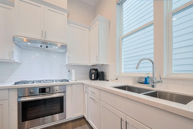 5308 S Capitol St, Houston, TX 77023 - kitchen with appliances with stainless steel finishes, under cabinet range hood, white cabinetry, backsplash, and light stone countertops