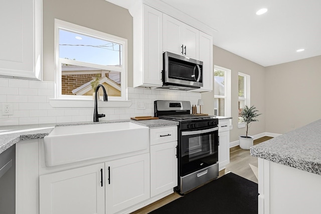 2346 Delafield St, Houston, TX 77023 - kitchen featuring stainless steel appliances, tasteful backsplash, light wood-style flooring, white cabinetry, and recessed lighting