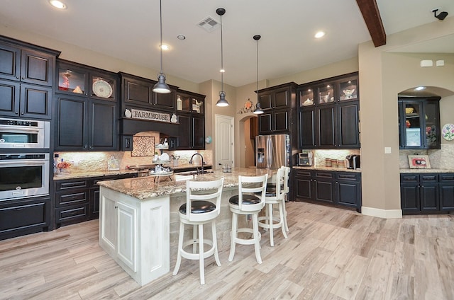 33215 Worthing Ln, Fulshear, TX 77441 - kitchen featuring arched walkways, tasteful backsplash, appliances with stainless steel finishes, light wood-style floors, and beam ceiling
